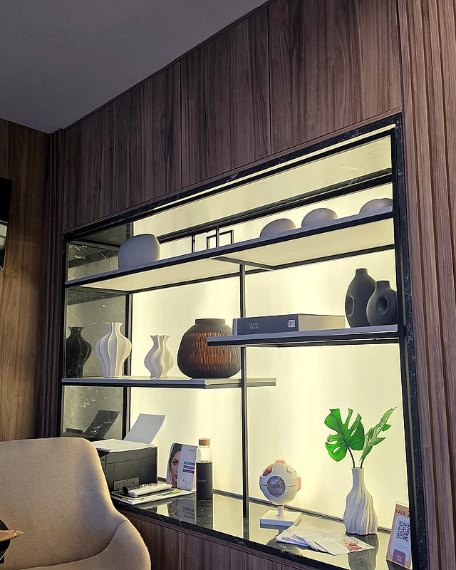 Nicho iluminado da recepção, com prateleiras de vasos, livros e um modelo anatômico do olho